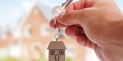Holding house keys on house shaped keychain in front of a new home
